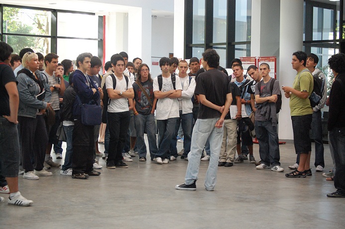 Imagen alumno exponiendo rodeado de otros alumnos escuchando la exposición